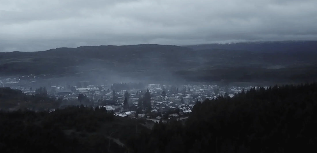 Paisaje de pueblo entre montañas con cielo nublado y niebla matutina